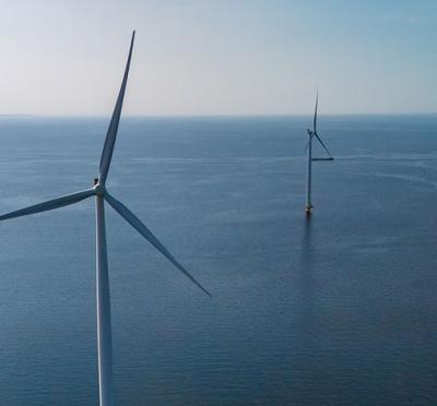 Four wind turbines in the ocean with the horizon in the distance. 